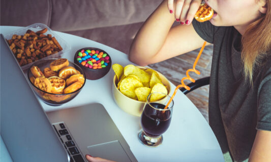 Woman stress eating in front of a laptop. Eating junk food including chips, cookies, candy
